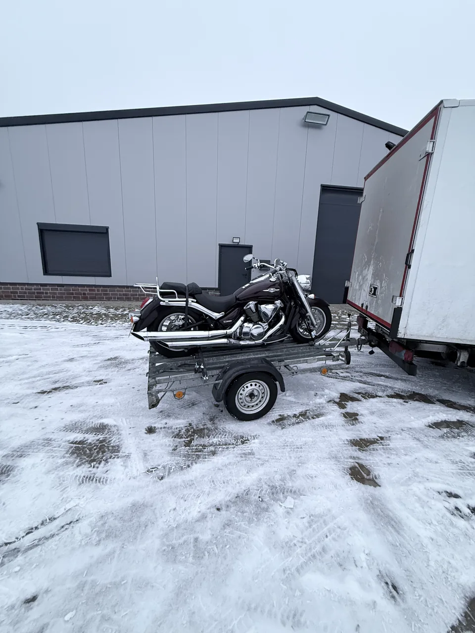 Herzig Dienstleistungen: Ein Motorrad steht auf dem Transportanhänger hinter dem Möbeltransporter.