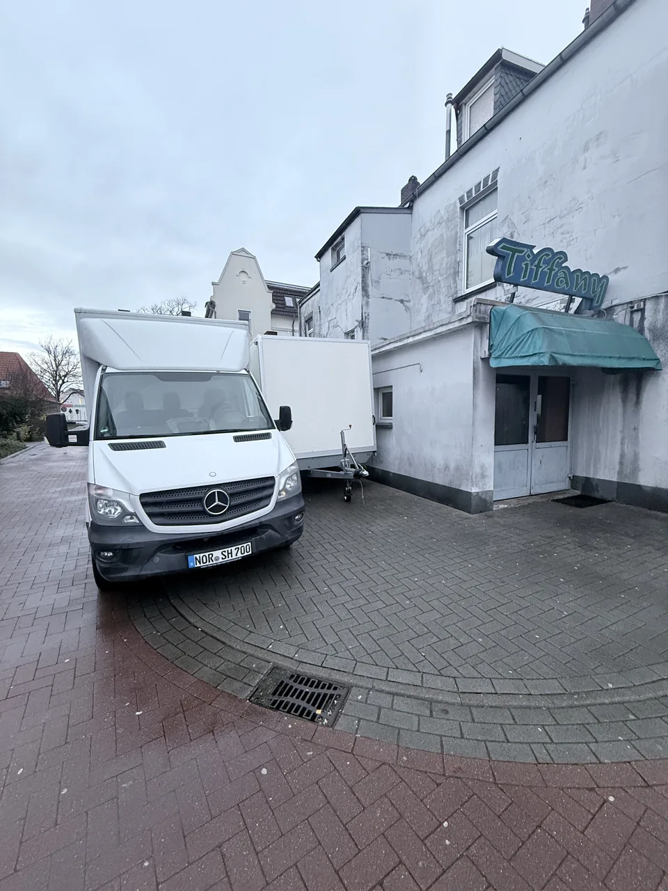 Herzig Dienstleistungen: Weißer Transporter und Kofferanhänger während eines Einsatzes am Gebäude.