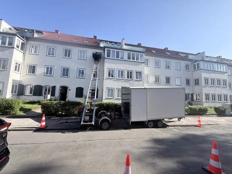Möbellift neben einem Umzugswagen vor einem Mehrfamilienhaus mit abgesperrtem Ladebereich